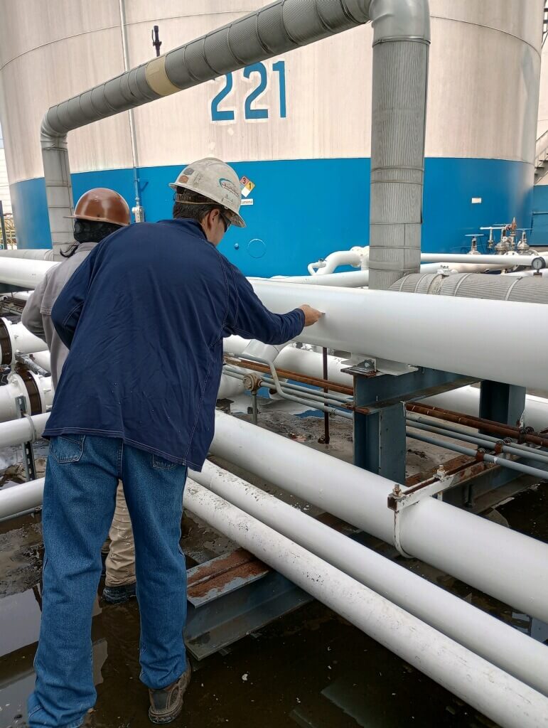 An inspector checks the wet film thickness of a new protective coating applied to steel piping at a liquid terminal.