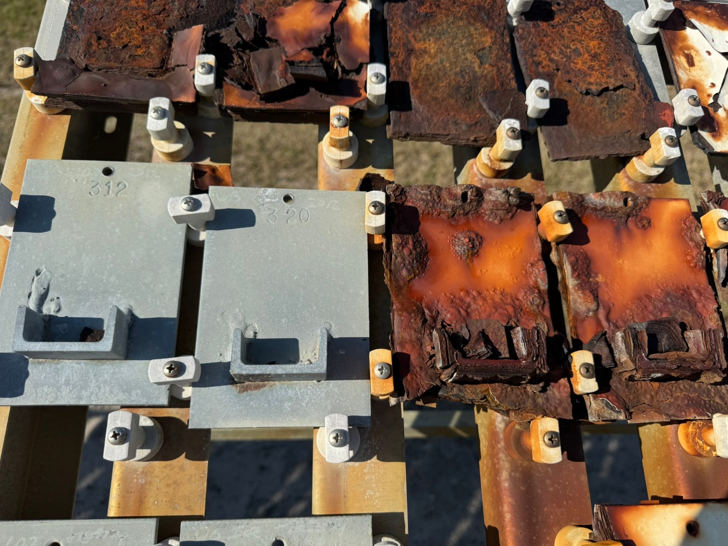 Coated steel coupons in various conditions are shown at an outdoor coastal corrosion test site.