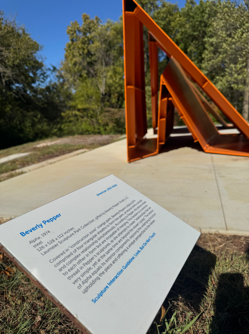 Focused image of a sculpture’s informational plaque with the sculpture in a blurred view behind it.